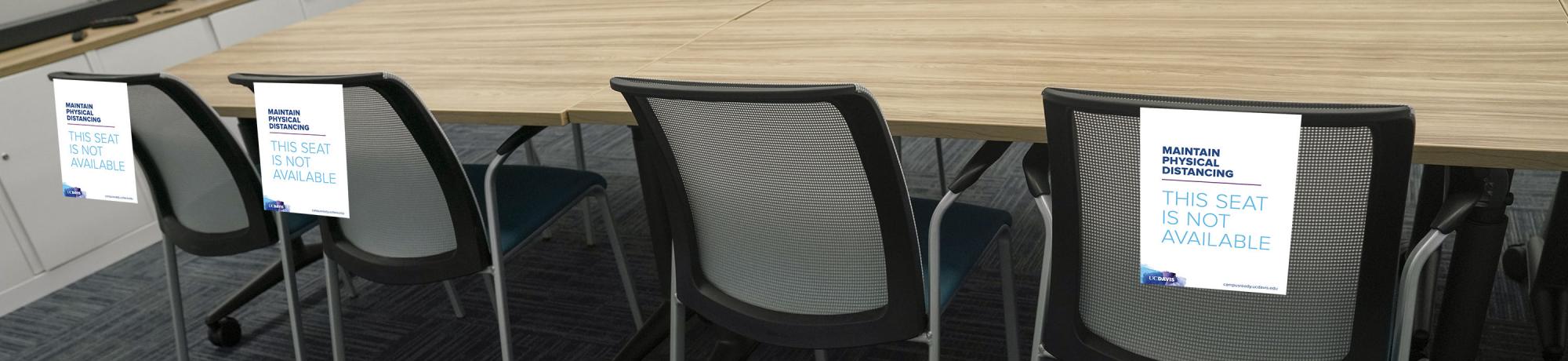 chairs in conference room with signs, "Maintain physical distancing: This seat is not available"
